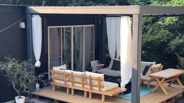 Une terrasse en bois avec un canapé et une table, entourée d’un jardin agrémenté d’une plante en pot et d’un petit arbre.