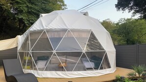 Une structure en forme de dôme géodésique, avec un lit et un espace salon à l’intérieur, le tout entouré d’une terrasse.