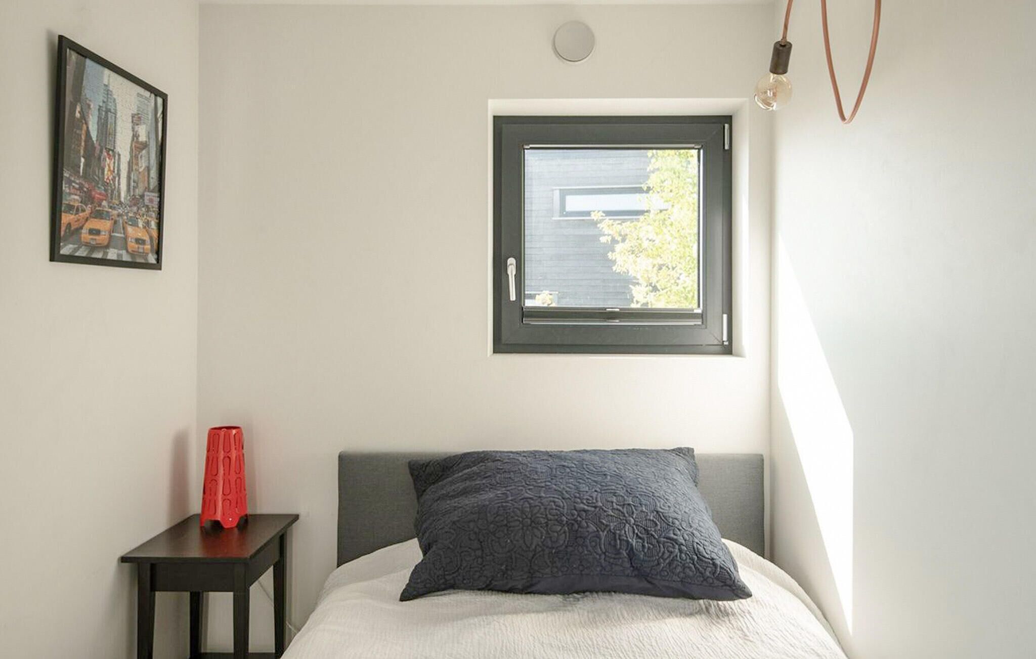 Une chambre à coucher avec un lit, une fenêtre, une table de chevet et un tableau encadré au mur.
