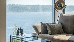 A modern living room with a large window offering a view of a body of water and a forested area. - 4 bedroom nice home in Sætre (Sætre)