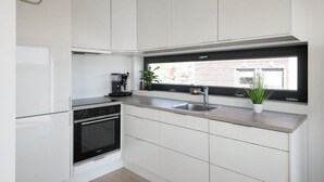 A modern kitchen with white cabinetry, a built-in oven, a coffee machine, a sink, and a window with a view of the outside. - 4 bedroom nice home in Sætre (Sætre)