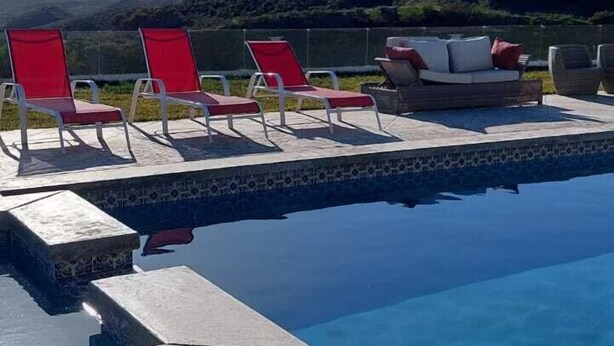 A pool area with red lounge chairs and a white sofa, surrounded by a tiled deck and a view of hills. - Cabañas hermosa vista Oceano-Montaña (Ensenada)