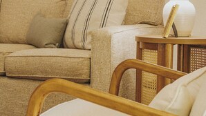 Una sala de estar con un sofá, una silla de madera, una lámpara y dos cuadros en la pared.