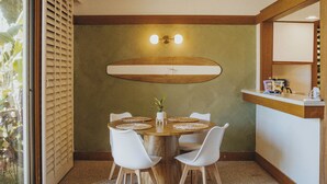 Un comedor con una mesa de madera, sillas blancas y un cuadro de un tabla de surf.