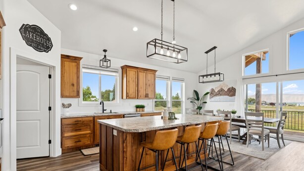 A modern kitchen with wooden cabinets, a large island with bar stools, and a view of the outdoors. - Modern Lakehouse l Slps 34 l Courts + Chefs Kitchen l Bear Lake Haven (Saint Charles)