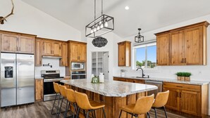 A modern kitchen with wooden cabinets, a large island with bar stools, stainless steel appliances, and a farmhouse-style pendant light. - Modern Lakehouse l Slps 34 l Courts + Chefs Kitchen l Bear Lake Haven (Saint Charles)