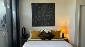 A bedroom with a large bed, a wall-mounted artwork, and a bedside lamp.