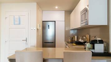 Una cocina compacta con un refrigerador integrado, un microondas y un fregadero con hervidor.