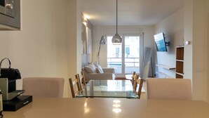 A modern kitchen with a glass dining table, wooden chairs, a built-in oven, and a TV mounted on the wall.