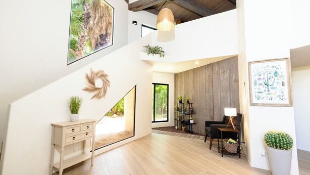 Een ruime woonkamer met een trap, houten vloeren, een eettafel met stoelen, een bank en een groot raam dat zorgt voor natuurlijk licht.