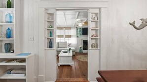 A hallway with white wooden walls, a white sofa, and a small table with decorative items. Shelves on either side hold various objects. - New List - Heated Pool Golf Cart Bikes Sleeps 12 (Santa Rosa Beach)
