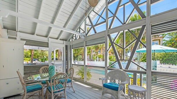 A covered outdoor area with wicker furniture and a glass table, overlooking a pool and greenery. - New List - Heated Pool Golf Cart Bikes Sleeps 12 (Santa Rosa Beach)