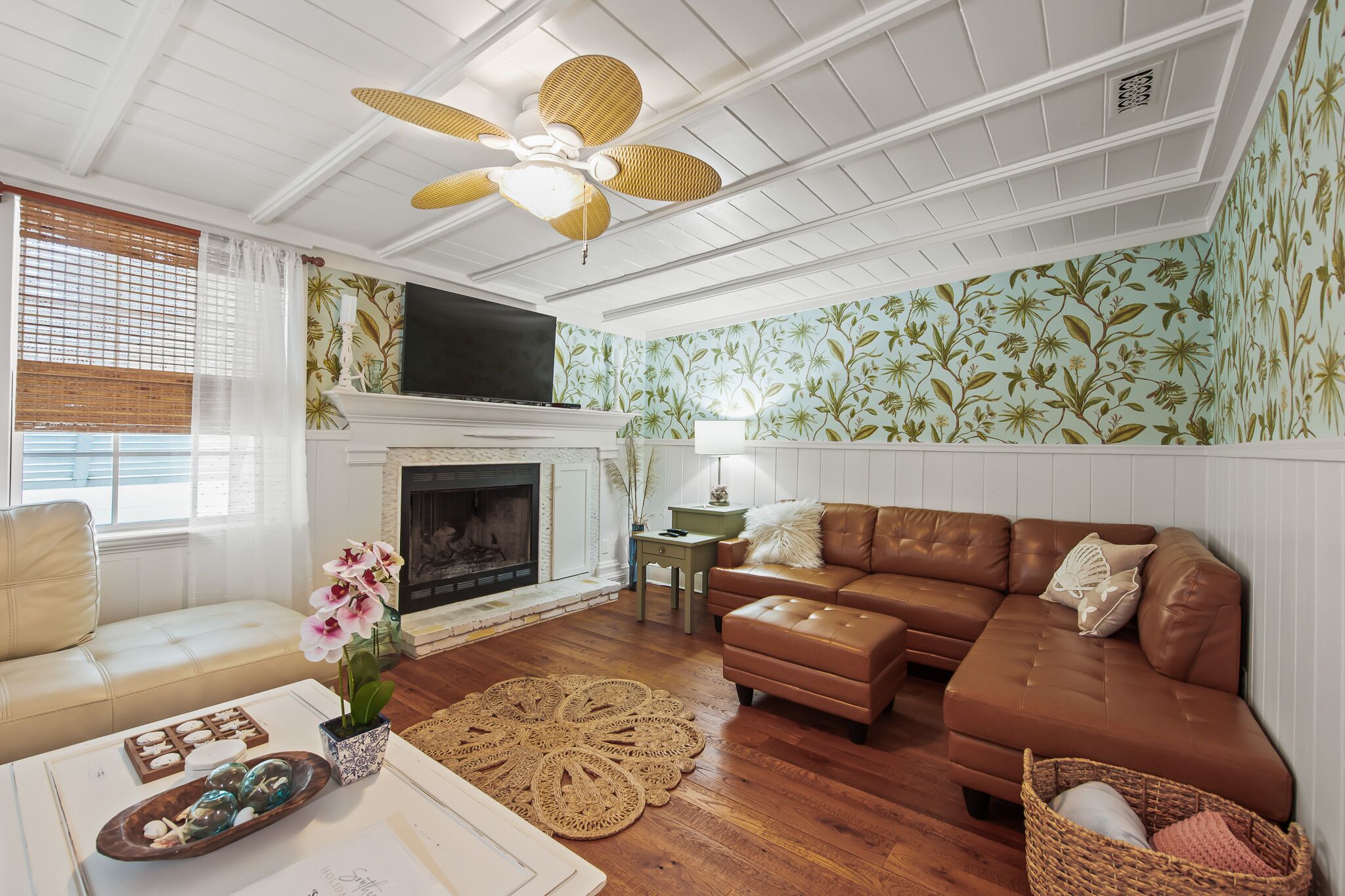 A living room with a fireplace, a brown leather sofa, a white coffee table, and a ceiling fan.