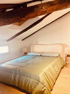Une chambre avec un plafond en pente, un lit recouvert d’une couette verte, deux lampes de chevet et une fenêtre.