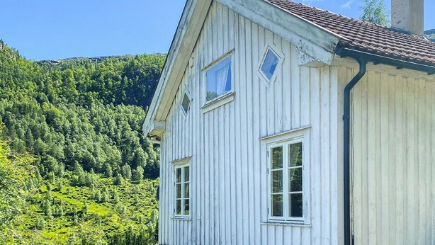 A white wooden house with a sloped roof and two windows, set against a backdrop of a forested hillside. - Stunning home in Tonstad with WiFi (Tonstad)