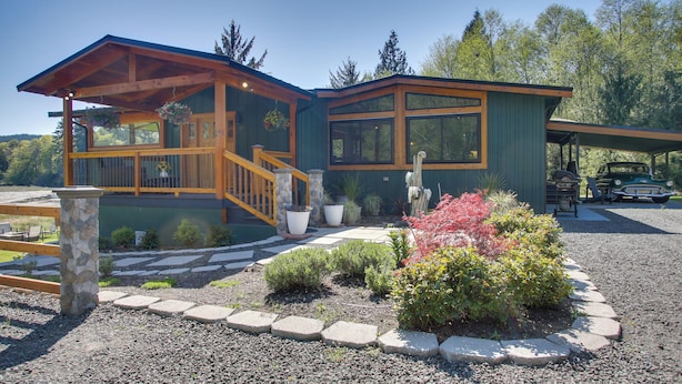 A two-story house with a wooden deck, large windows, and a stone pillar.