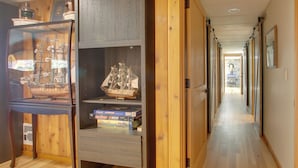 A hallway with wooden flooring, a display case with model ships, and a view into another room.