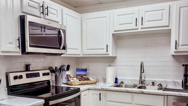 A modern kitchen with white cabinets, a microwave, stove, oven, and dishwasher.