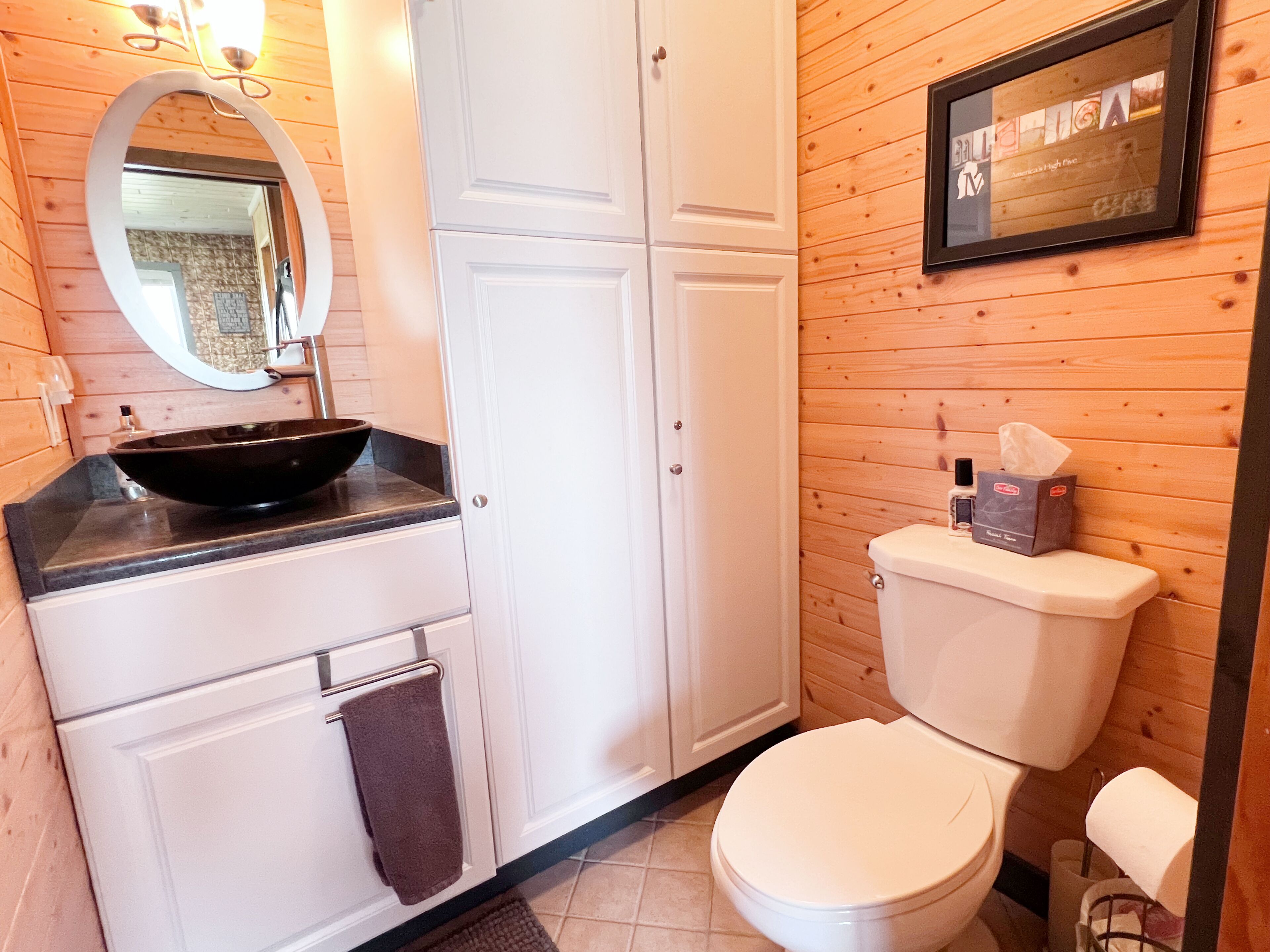 A bathroom with a black sink, white cabinets, a toilet, and a framed picture on the wall.