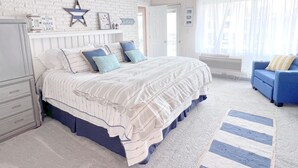A bedroom with a white brick wall, a bed with striped bedding, a blue and white striped rug, and a blue sofa.