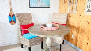 A wicker dining set with a round table and two chairs, each with a cushion.