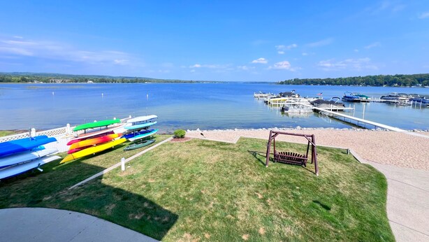 A lakeside view with a grassy area, a swing set, and colorful kayaks docked at the marina.