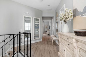 A hallway with a staircase, a white dresser, and a vase of flowers.