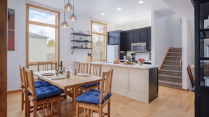 A modern kitchen with a central island, wooden dining table with blue cushions, and a staircase leading to a dark room. - RMR: Windflower 2121 Condo in The Aspens/Wilson,WY (Wilson)