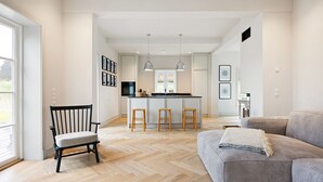 A modern kitchen with a central island, bar stools, pendant lights, and a dining area with a sofa and a chair. - Dünen.Way, Germany (List auf Sylt)