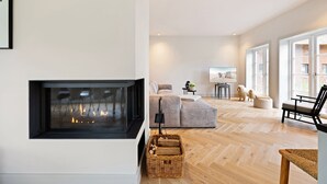 A modern living room with a fireplace, a sofa, a TV, and a large window. - Dünen.Way, Germany (List auf Sylt)