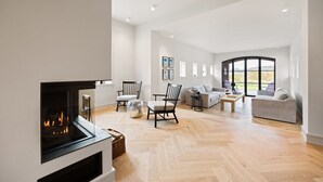 A spacious living room with a fireplace, wooden flooring, and a large window offering a view of the outdoors.