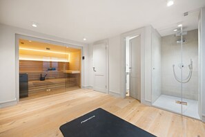 A modern bathroom with a glass shower enclosure, a wooden vanity, and a black exercise mat on the floor. - Heide.Way, Germany (List auf Sylt)