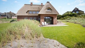 A thatched-roof house with a brick extension, a grassy lawn, and a sandy area in front.