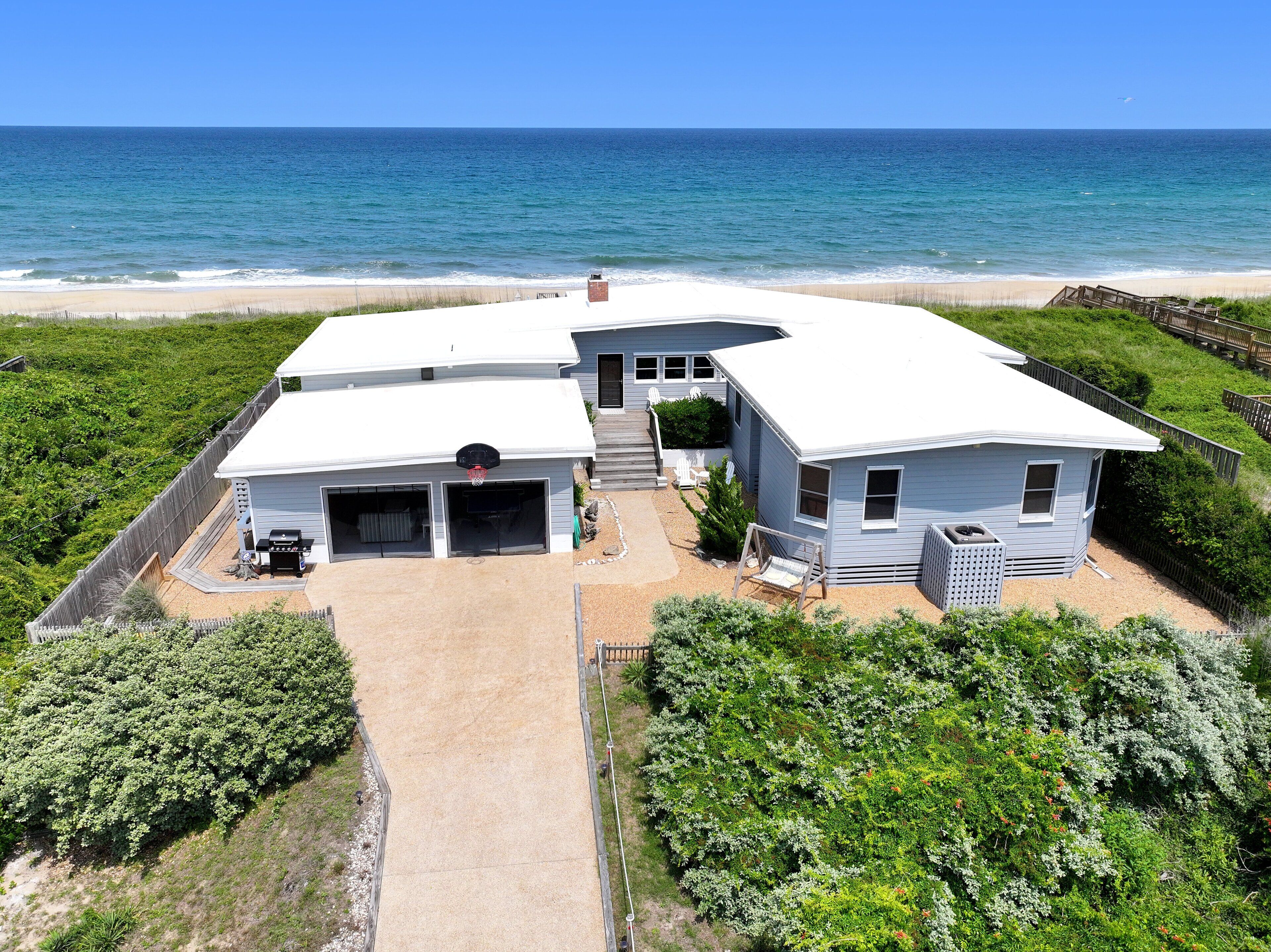 A two-story house with a garage, a basketball hoop, and a view of the ocean.
