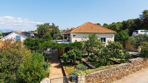A residential area with a house featuring a tiled roof, a balcony, and a garden with various plants and a stone wall. - 1 bedroom gorgeous apartment in Necujam (Necujam)