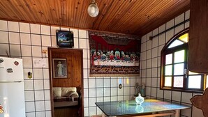 Een keuken met een houten plafond, een betegelde vloer, een koelkast, een tafel met een bank en een schilderij van 'De laatste avondmaal' aan de muur.