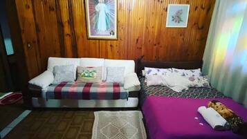 Una habitación con paredes de madera, un sofá, una cama con colcha morada y un cuadro enmarcado en la pared.