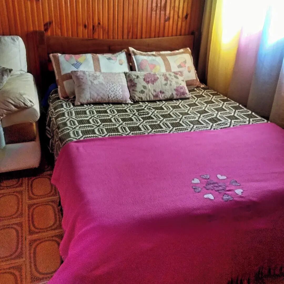 A bedroom with a wooden headboard, patterned bedding, and a pink blanket.
