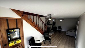 A living room with a wooden staircase, a fireplace, and a Pac-Man arcade game.