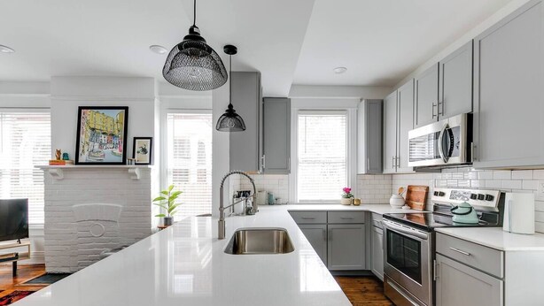 Een moderne keuken met een groot eiland, roestvrijstalen apparatuur en een witte spatwand.