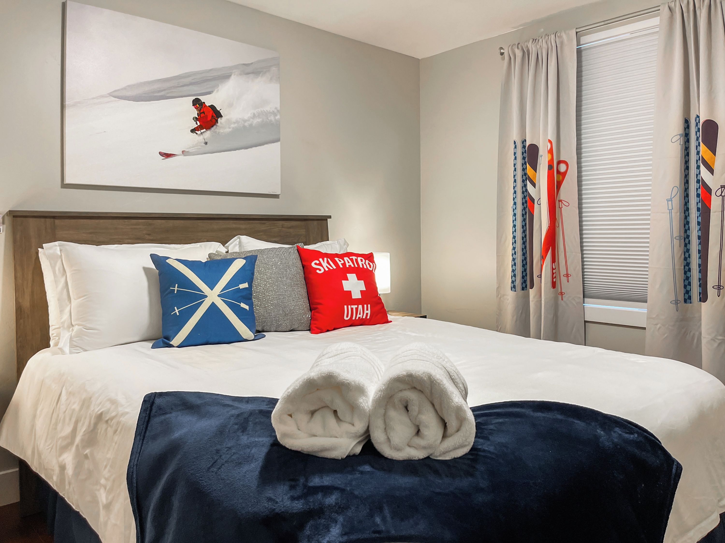 Habitación de hotel con cama, cabecero, un cuadro de un esquiador y cortinas con motivos de esquí.