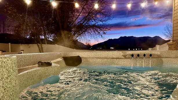 Een hottub met uitzicht op bergen in de schemering, omringd door lichtjes en een houten terras.