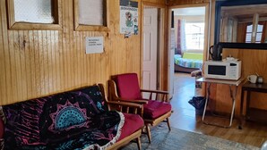 A cozy room with a wooden sofa, a red armchair, a small table with a microwave, and a rug.