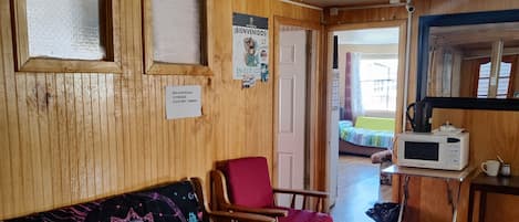Una habitación acogedora con un sofá de madera, un sillón rojo, una mesita con microondas y una alfombra.