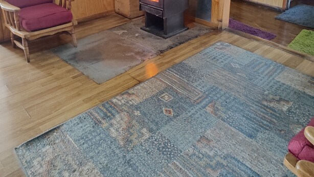 A cozy room with a wood-burning stove, wooden walls, a mirror, a wooden chair, and a rug.