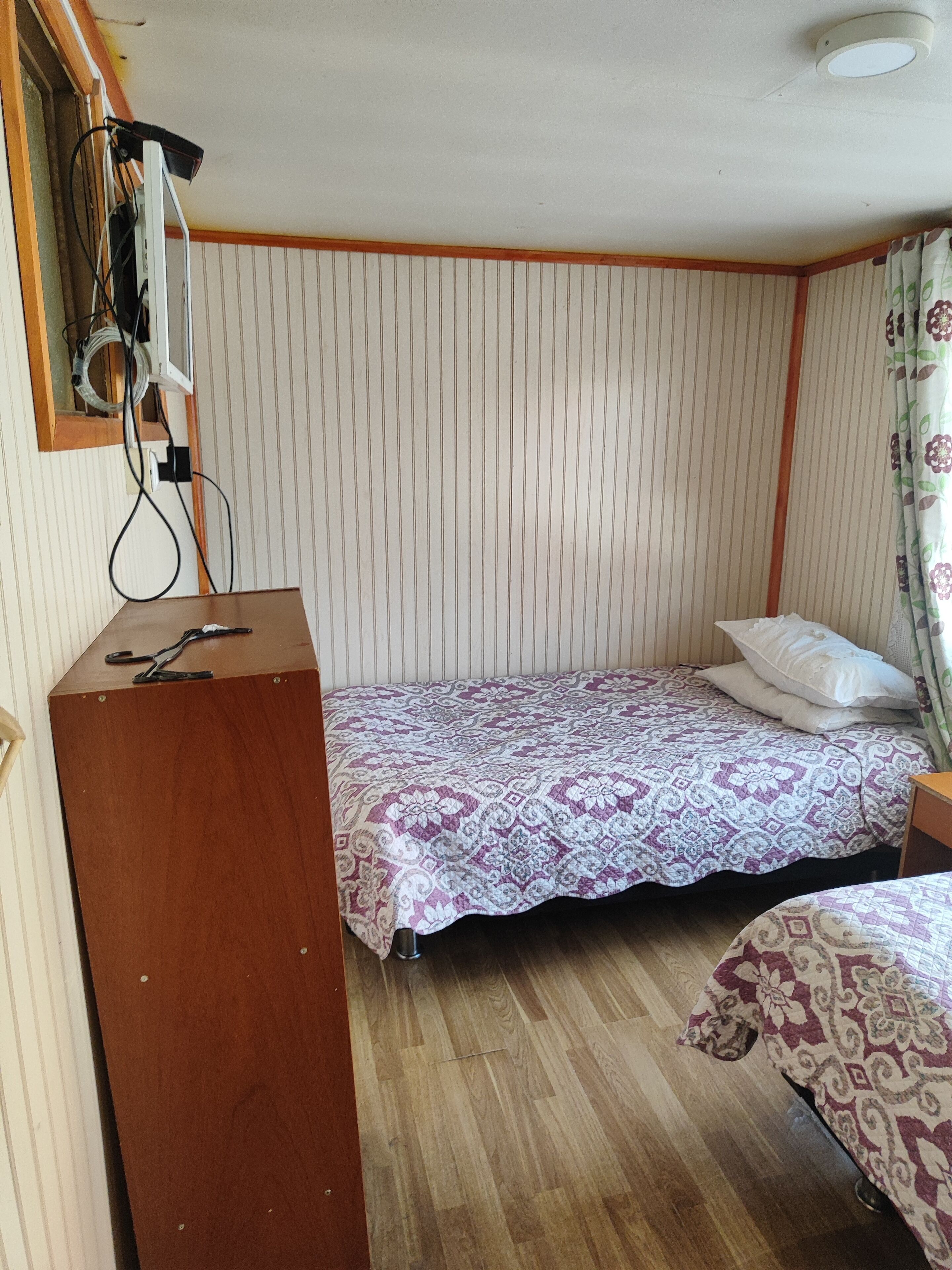 Une petite pièce avec un lit simple, un bureau en bois et une fenêtre avec des stores.