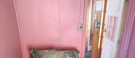 Una habitación pequeña con una cama individual, pared rosa y puerta de madera.