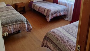 A room with three beds, wooden walls, a small wooden nightstand, and a window with sheer curtains.
