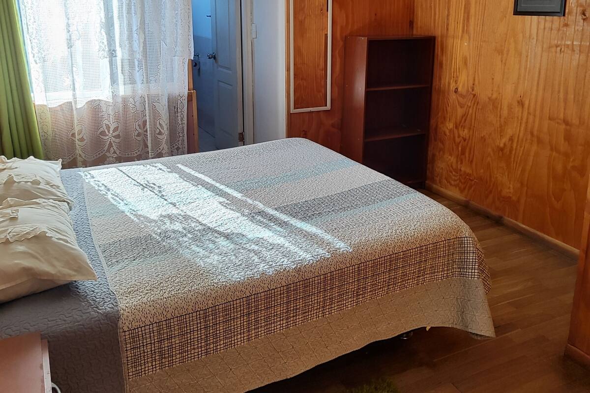 Una habitación con una cama, un armario de madera, un tapete verde y una puerta que da a otra habitación.