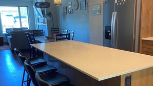 A modern kitchen with a central island, bar stools, wooden cabinets, and a stainless steel refrigerator. - Beautiful Echo Landing Retreat, Sleeps 8, 3 Bdrm, Private Hot Tub, Ski In/Out  (Sun Peaks)